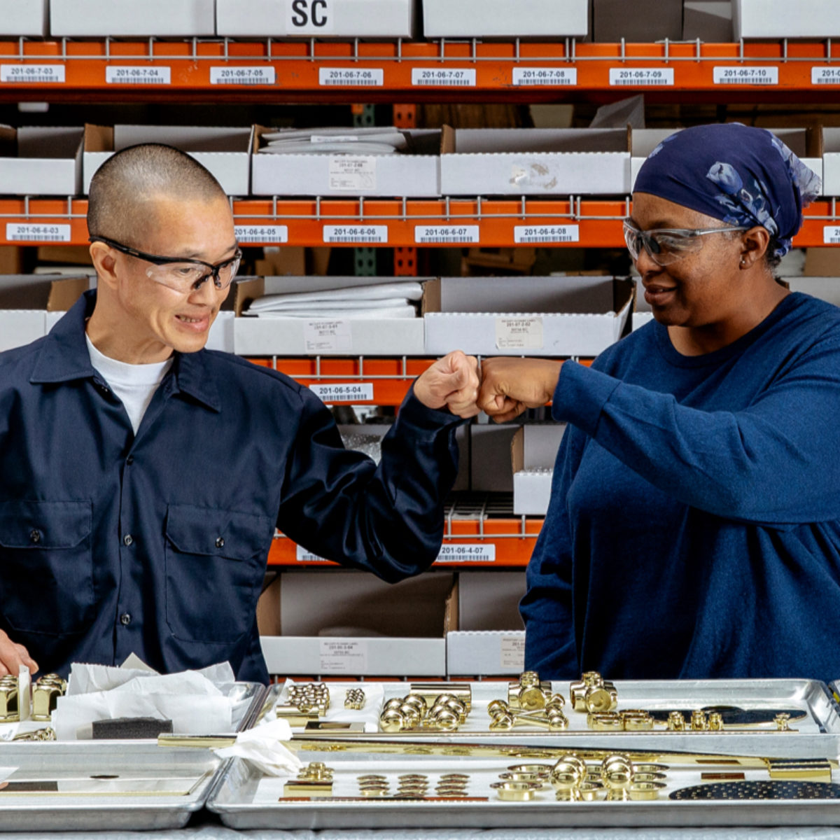 California Faucets employees fist bump over trays of brass parts